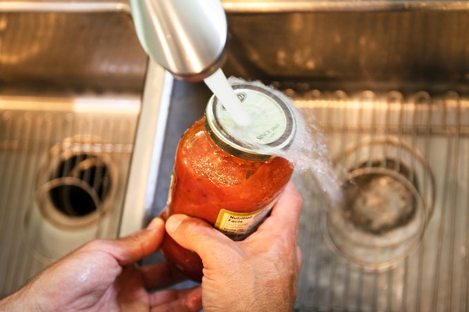man holding a jar under hot water to get it open