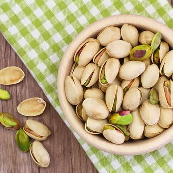 Pistachio nuts in wooden bowl on checkered cloth