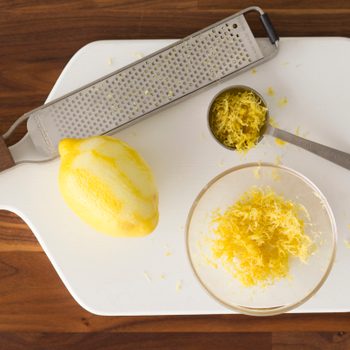 Lemon, bowl of lemon zest, spoon and grater together