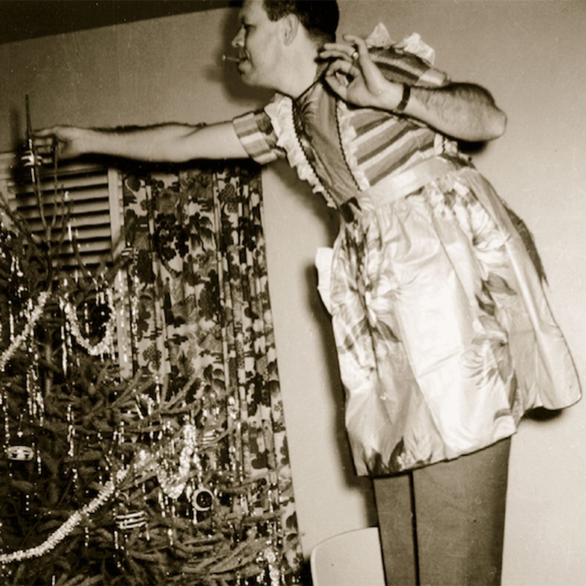 Man wearing a festive apron adding ornaments to a Christmas tree