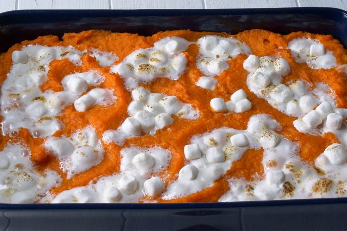 A large baking dish filled with fluffy mashed sweet potatoes topped with toasted mini marshmallows. The dish sits on a white surface, and the marshmallows are slightly browned, giving a caramelized appearance against the vibrant orange sweet potatoes.