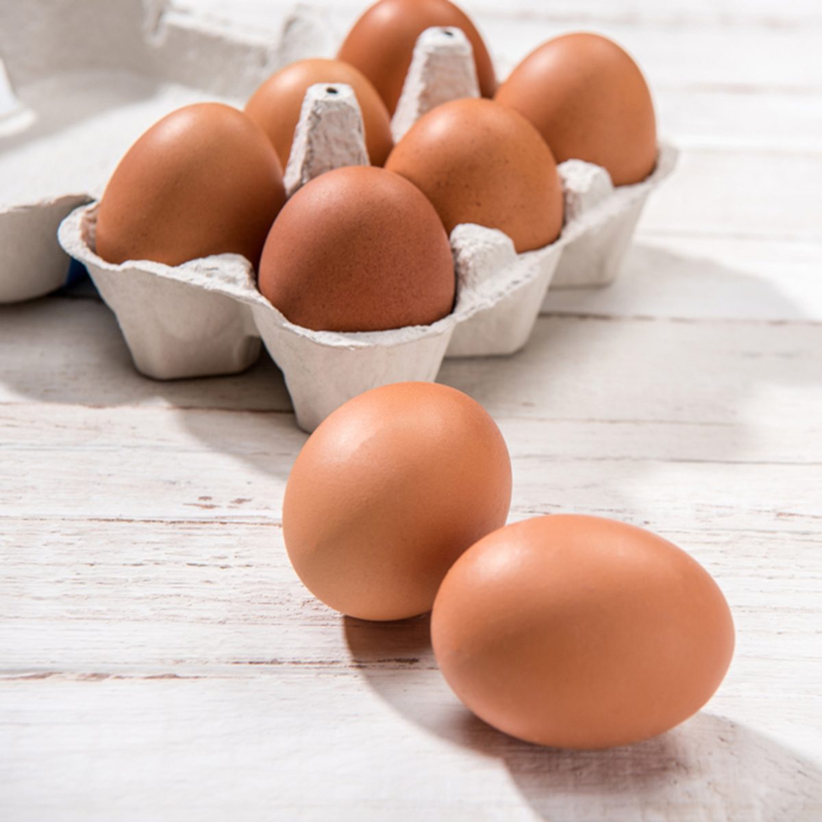 Close-up view of raw chicken eggs in egg box on white wooden background