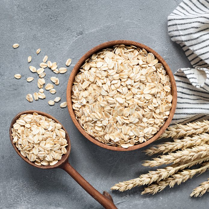 Oats, rolled oats or oat flakes in wooden bowl and wooden spoon. Top view. Healthy grains, low carb diet food