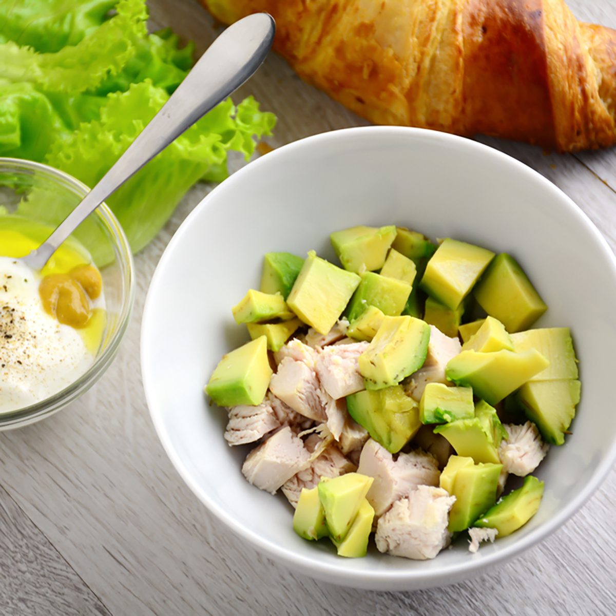 Preparing chicken avocado salad with light yogurt dressing on gray wooden table.