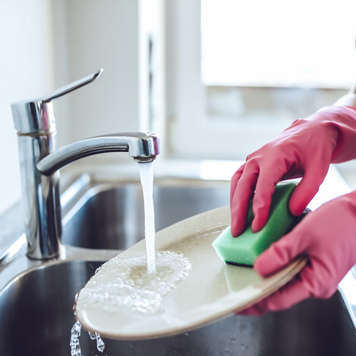 Cropped image of attractive young woman is washing dishes while doing cleaning at home