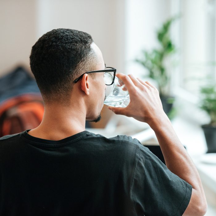 Back view of a young african man drinking water out of glass during coffee break at cafe