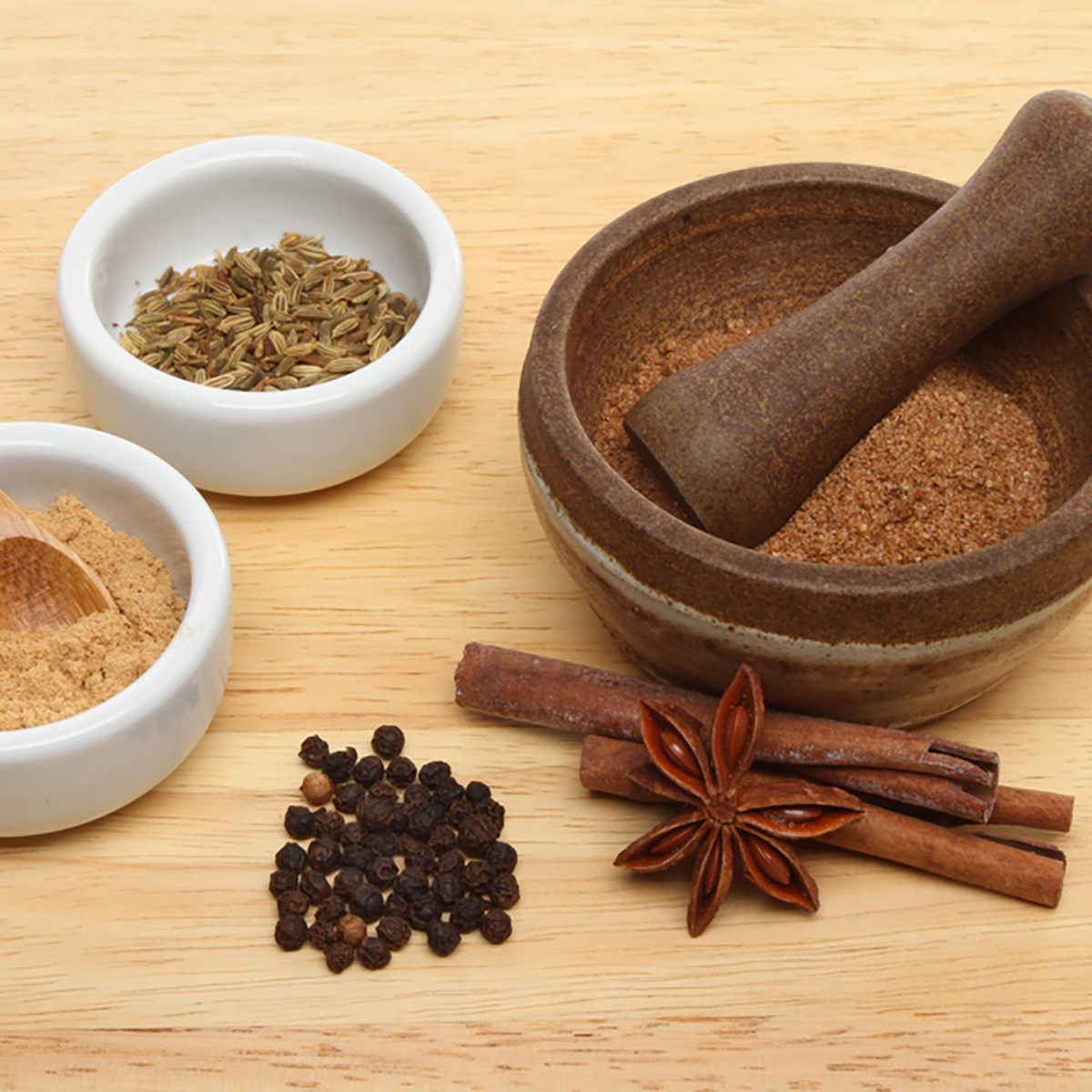 Ingredients for Chinese five spice with ramekins and a pestle and mortar on a wooden board