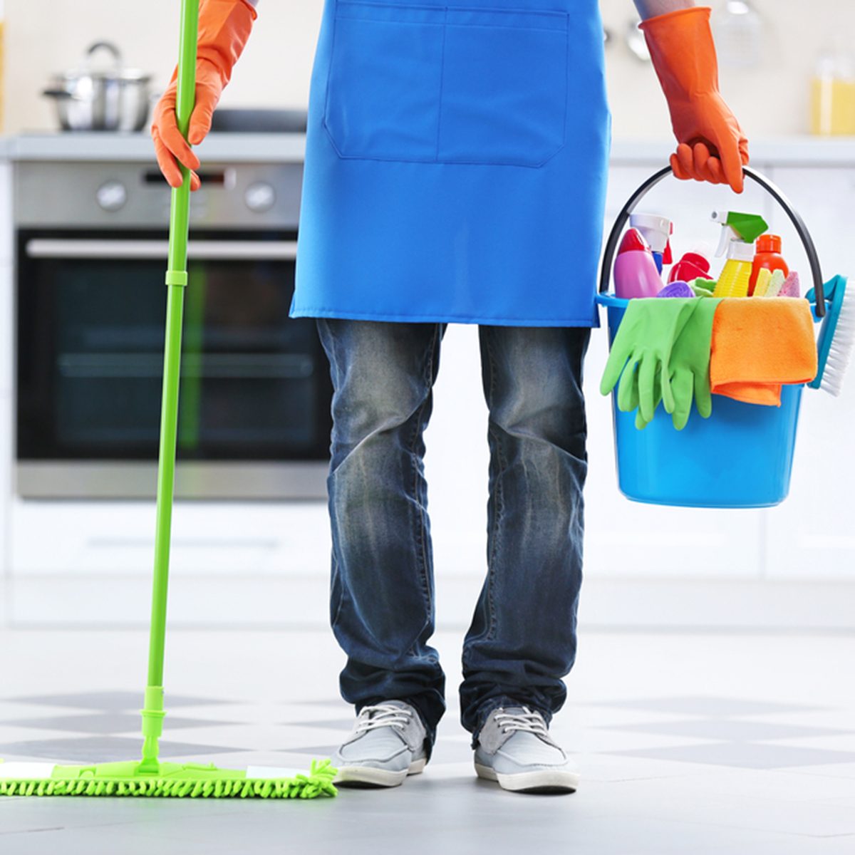 Man holding mop and plastic bucket with brushes, gloves and detergents in the kitchen