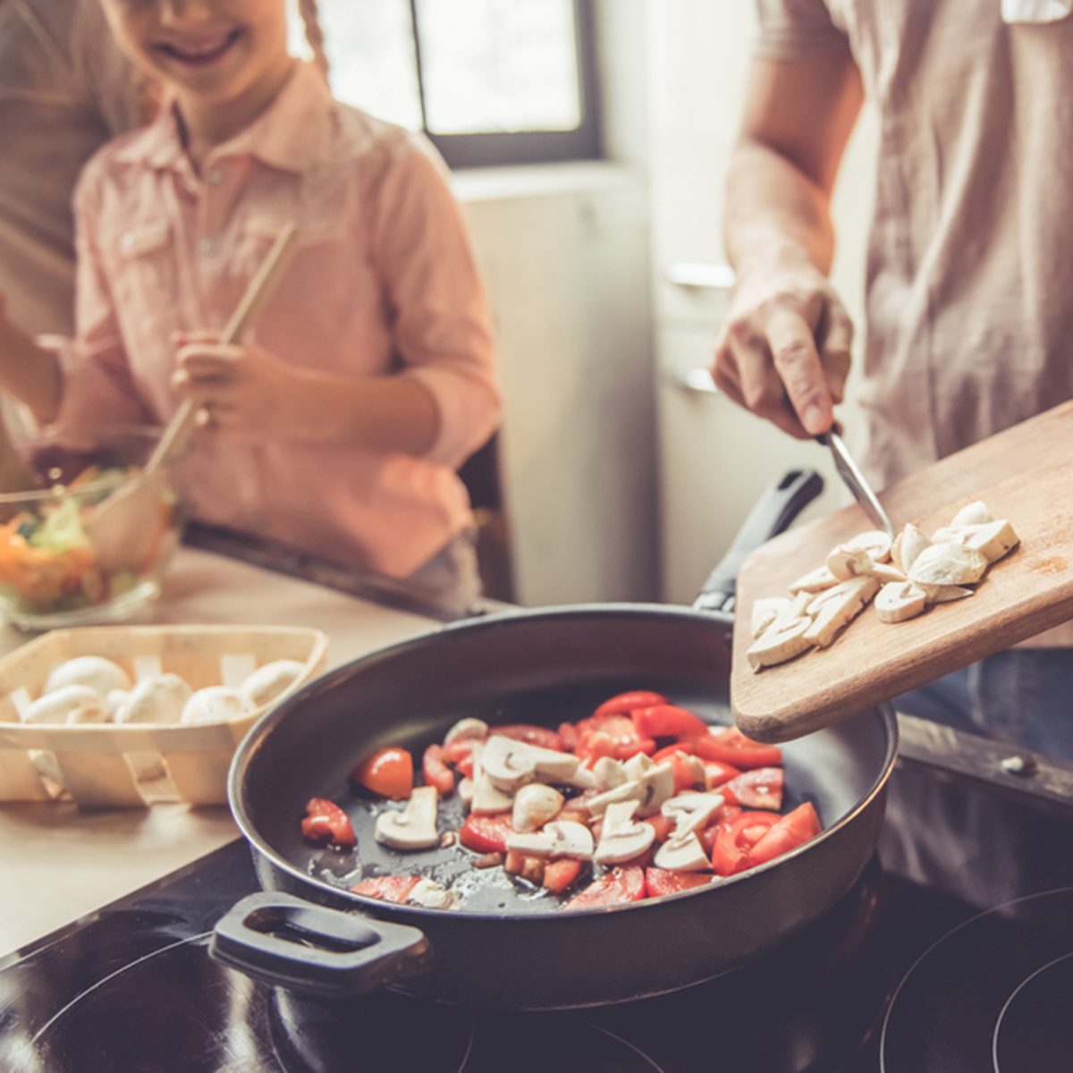 Cropped image of cute little girl and her beautiful parents cooking together in kitchen at home