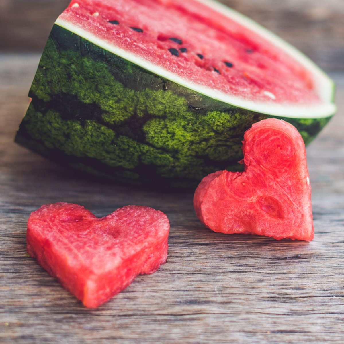 Healthy watermelon smoothie with mint, a piece of watermelon, hearts and a striped straw on a wood background.