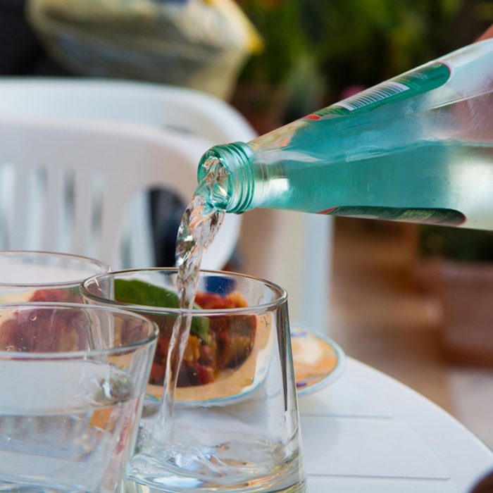 Waiter pouring mineral water from the glass bottle into a glass