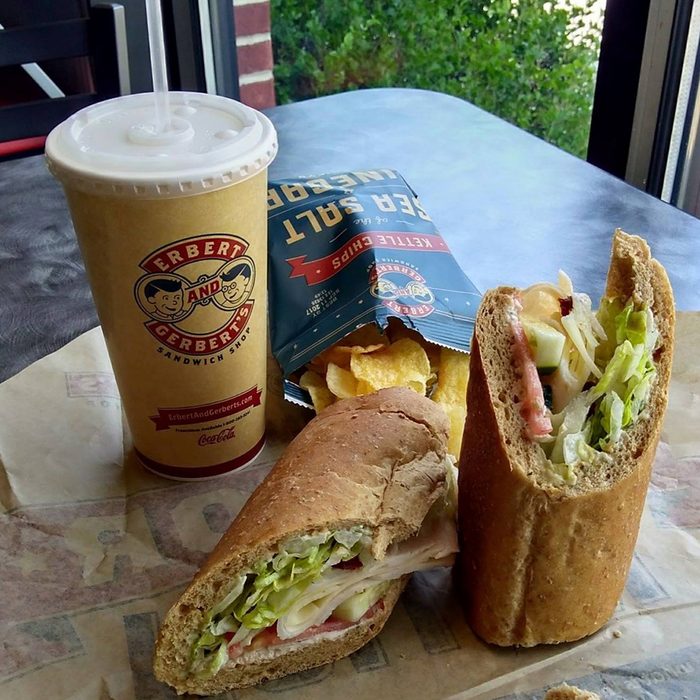 Sandwich cut in half beside fries and a drink