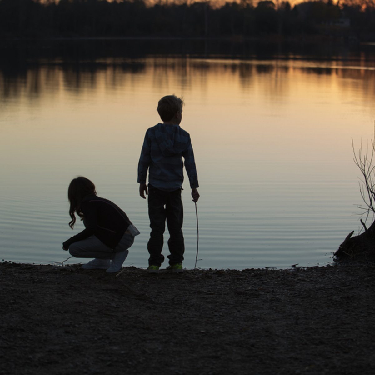 Silhouette of kids playing near the water on sunset