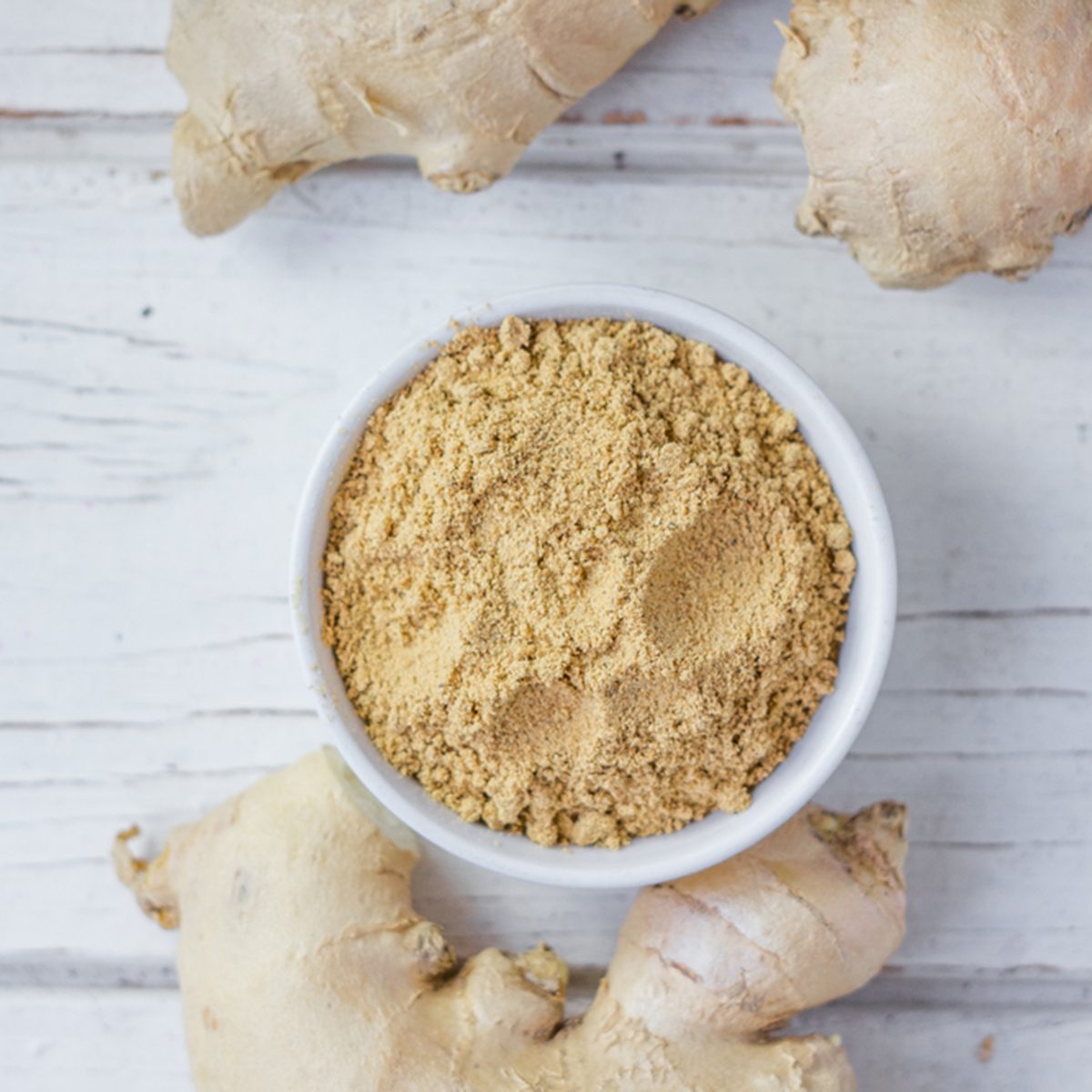 Grounded ginger and ginger root on white wooden surface.