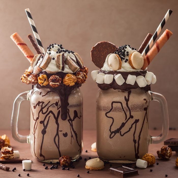 Chocolate milkshake with ice cream and with whipped cream, marshmallow, sweet popcorn, cookies, waffles, served in glass mason jar.