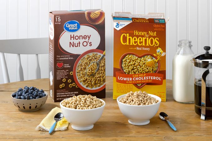 General Mills' Honey Nut Cheerios and Walmart's Great Value Honey Nut O's on a table with milk, coffee and blueberries