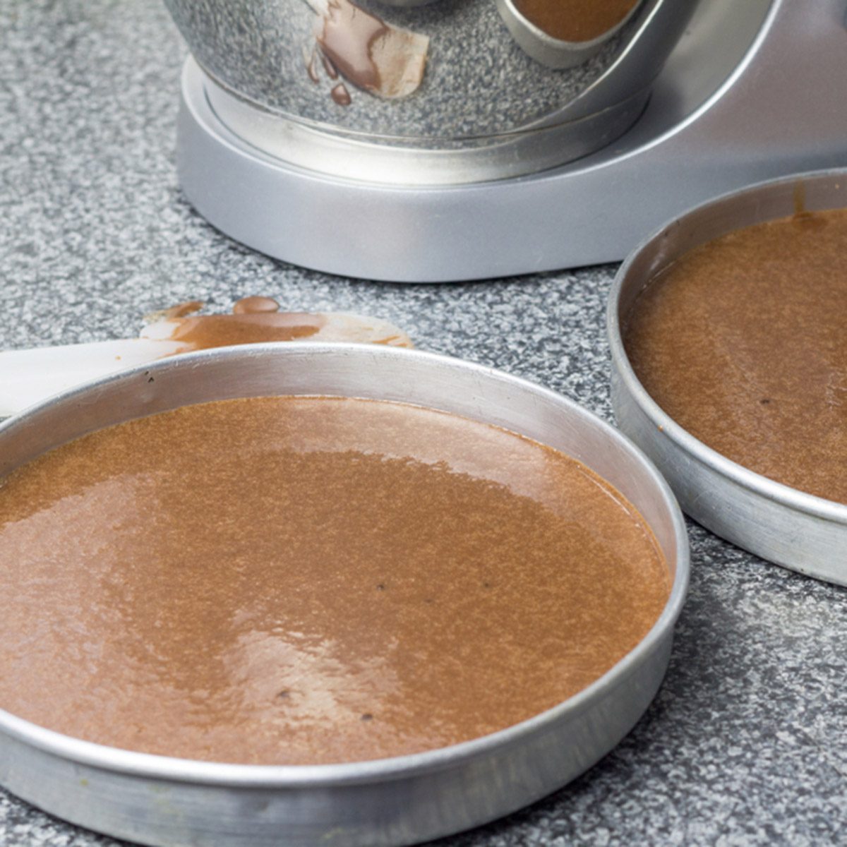 Cake pans with chocolate batter and mixer in background