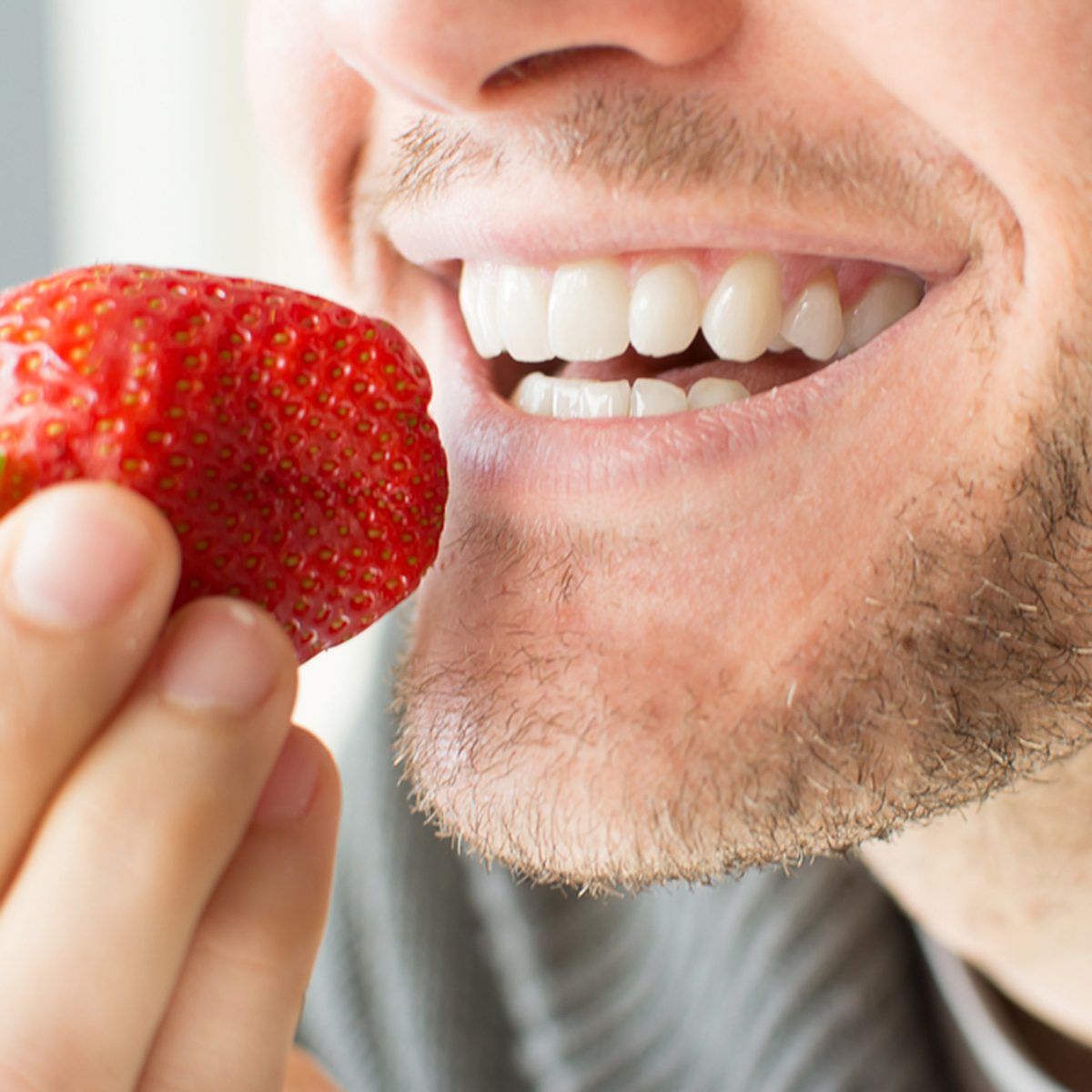 Young man holding a strawberry and smiling