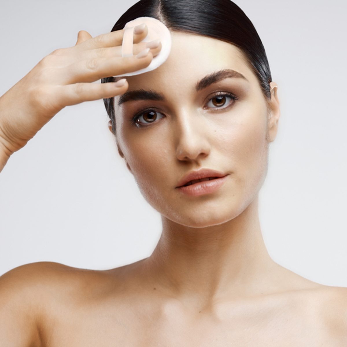 A beautiful woman wipes her face with a cotton pad and bare shoulders