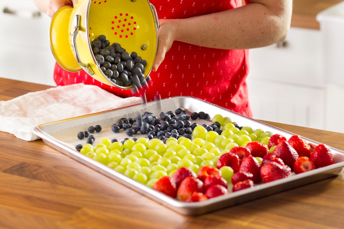 A person transferring just-washed berries and grapes from a collander to a baking sheet.