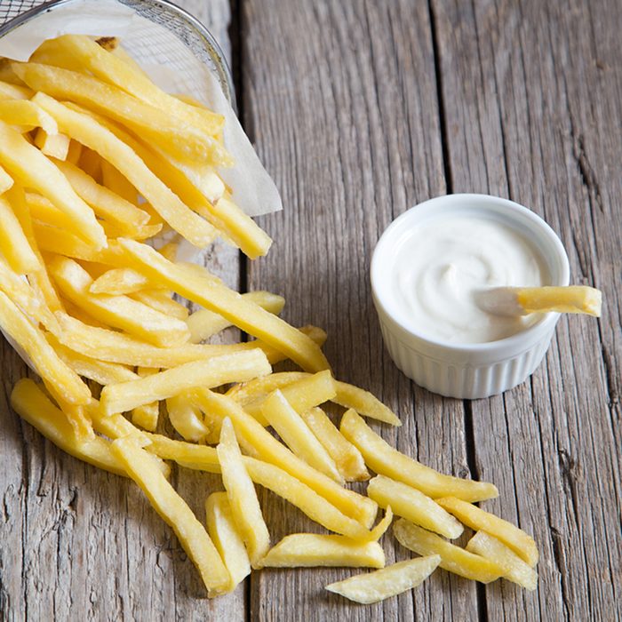 French fries in metal basket with mayonnaise on wood table