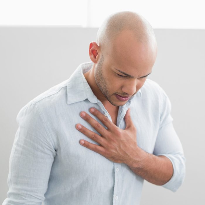 Casual young man with chest pain standing against white background