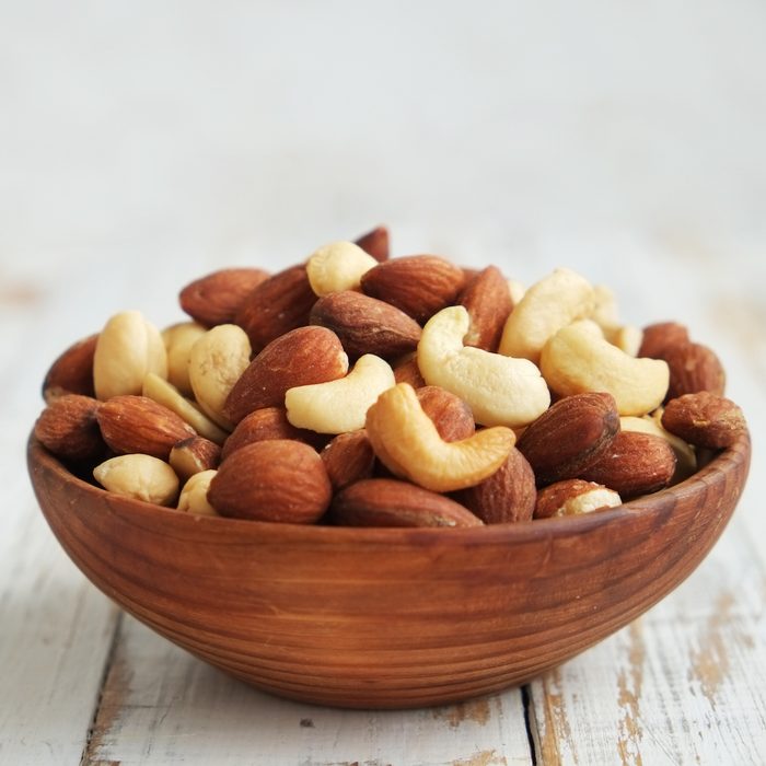 Mixed nuts in a bowl on a white wooden background.