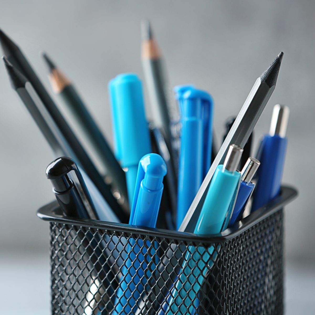 Pens and pencils in metal holder in front of wall background