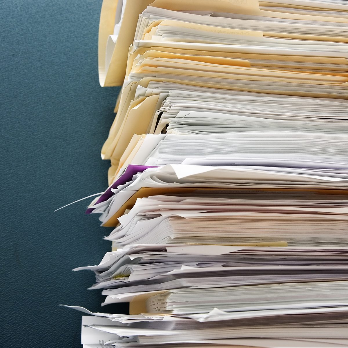 Pile of paperwork against a textured green cubicle wall