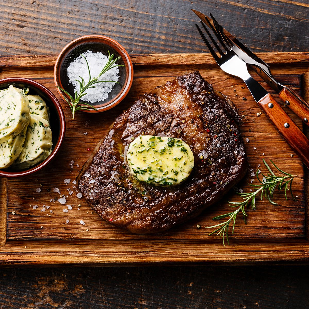Sliced grilled steak Ribeye with herb butter on cutting board on wooden background