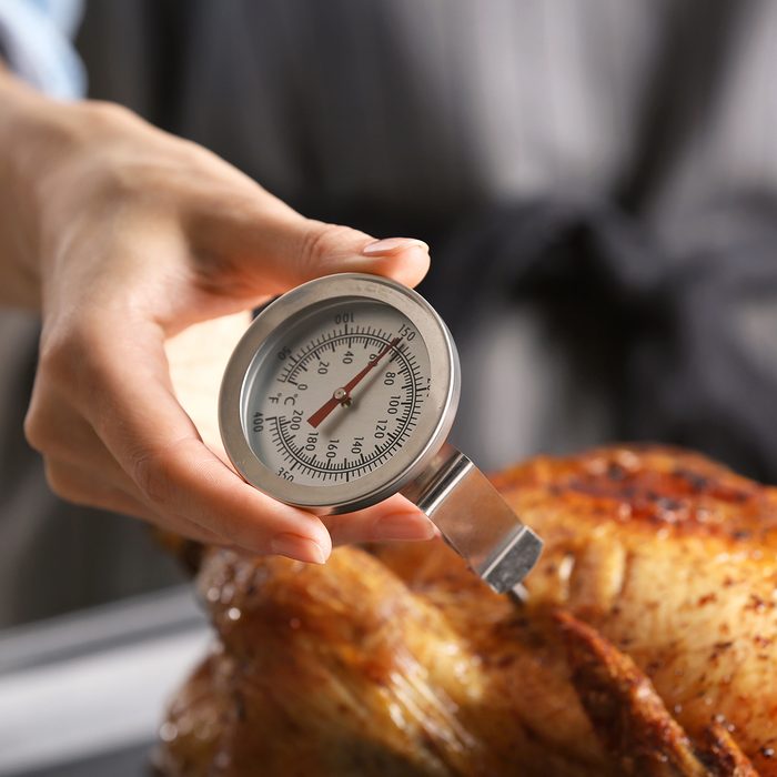Young woman measuring temperature of whole roasted turkey with meat thermometer