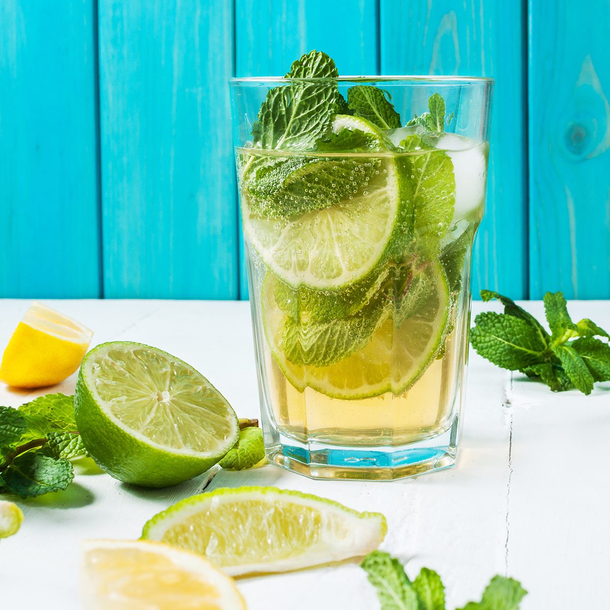 Mojito cocktail with lime and mint in highball glass on a wood table. Blue background.