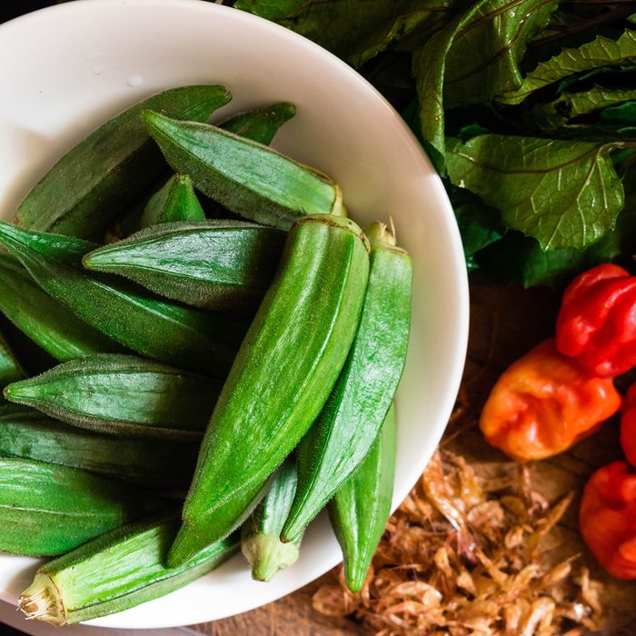 Top view of Farm fresh Raw Green Organic Okra or Lady Fingers in white bowl with red peppers, crayfish and pumpkin leaves or Nigerian ugwu leaves
