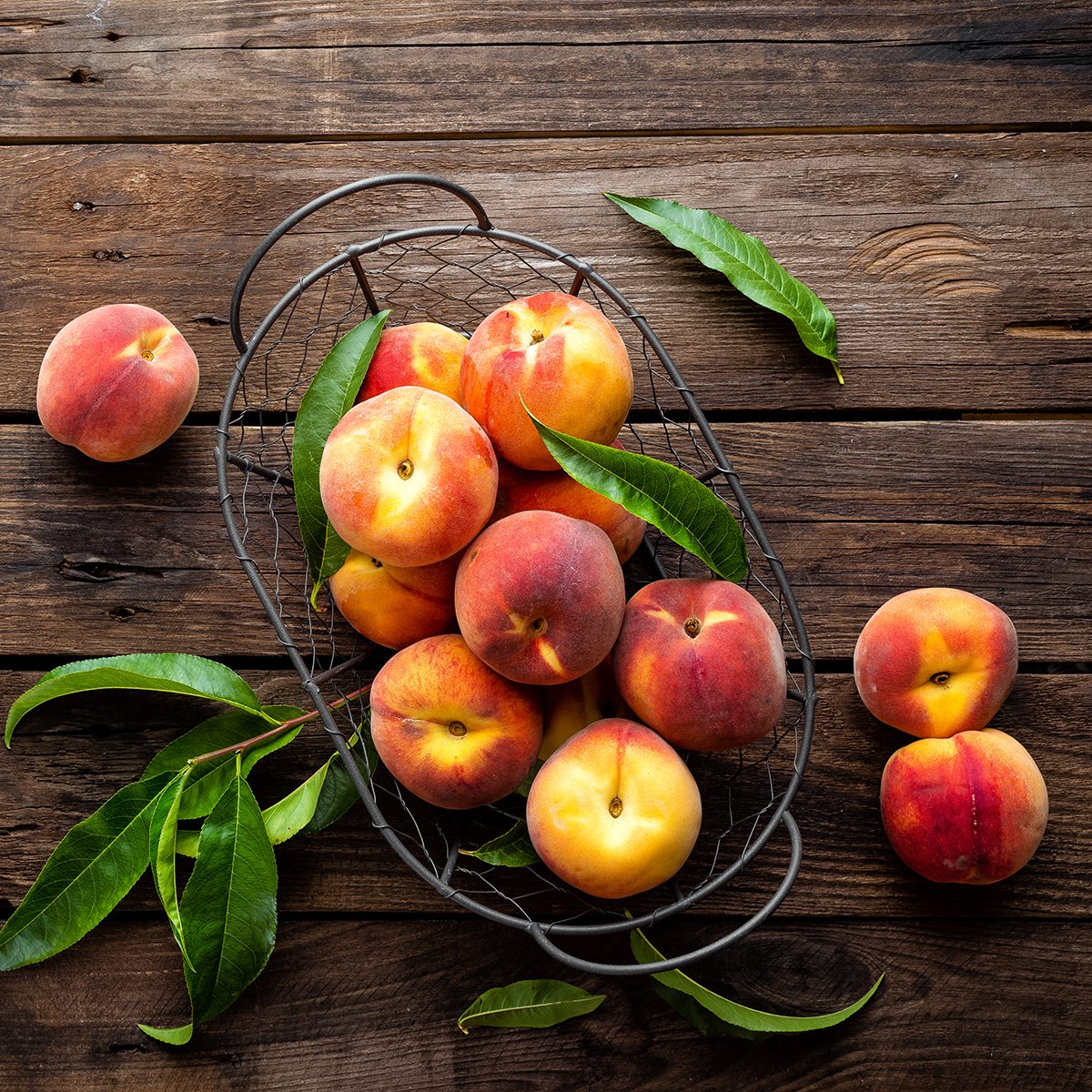 Fresh peaches fruits with leaves in basket on dark wooden rustic background