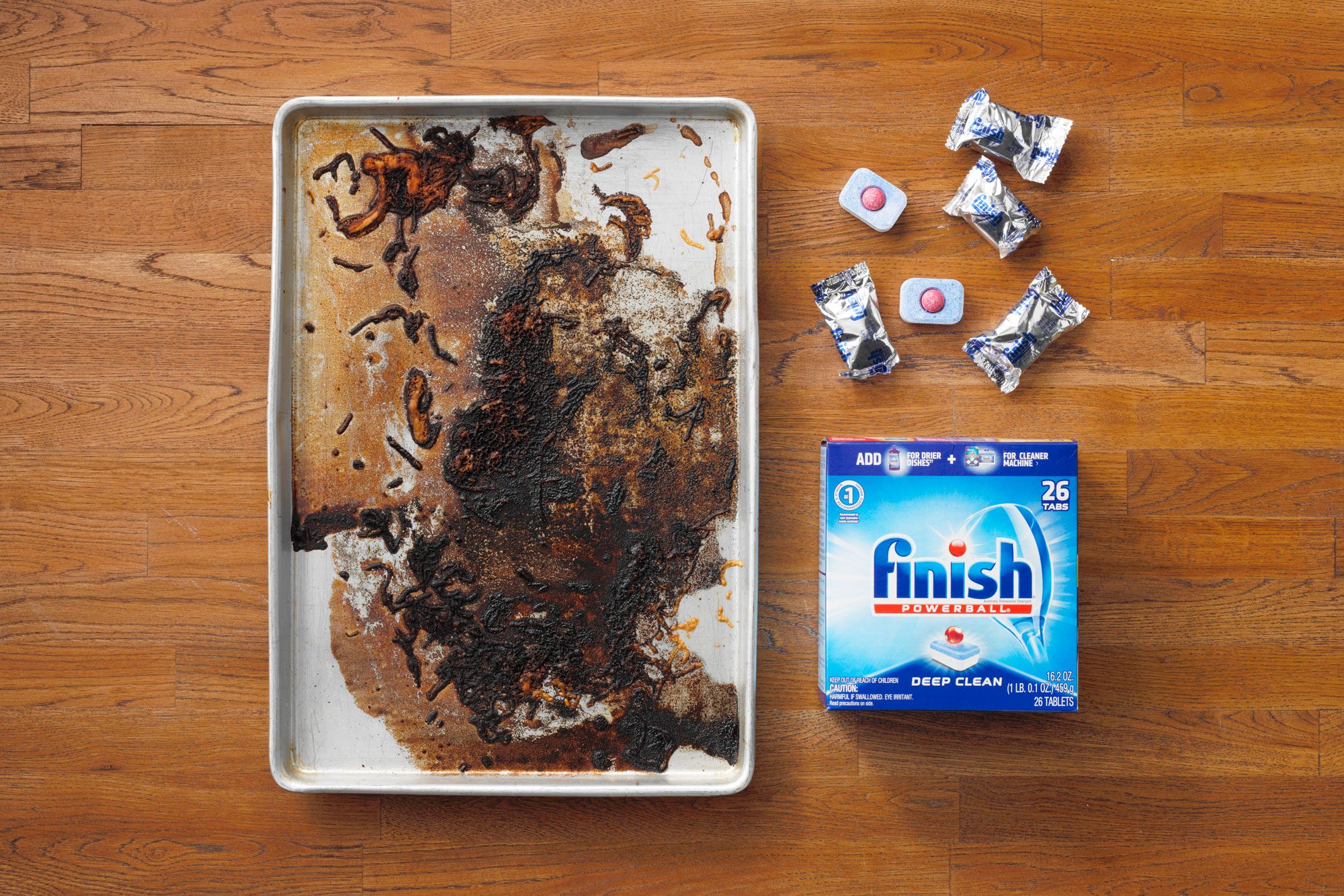 Dirty Baking Sheet next to Finish Powerball Deep Clean Dishwasher Tabs on wood butcher block background