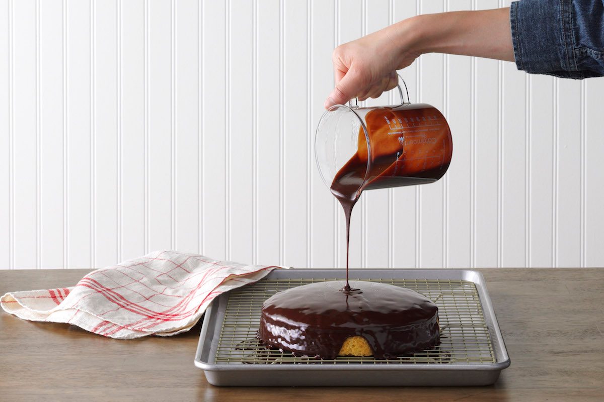 A person pouring homemade chocolate ganache over a cake.