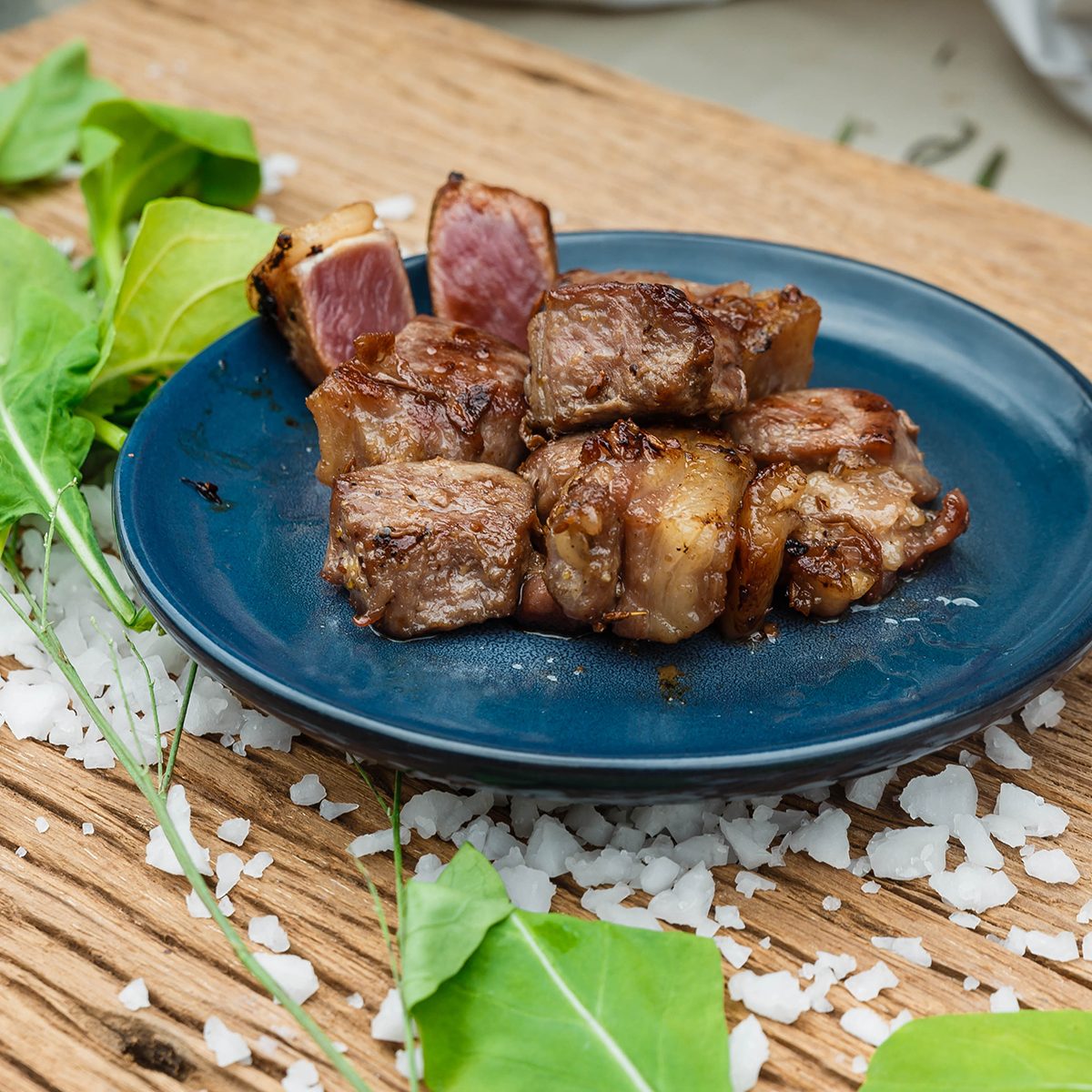 Medium Rare Fried Diced Marinated Beef on Blue Ceramic Plate on Wood Panel with Sea Salt and Vegetable Decorated.