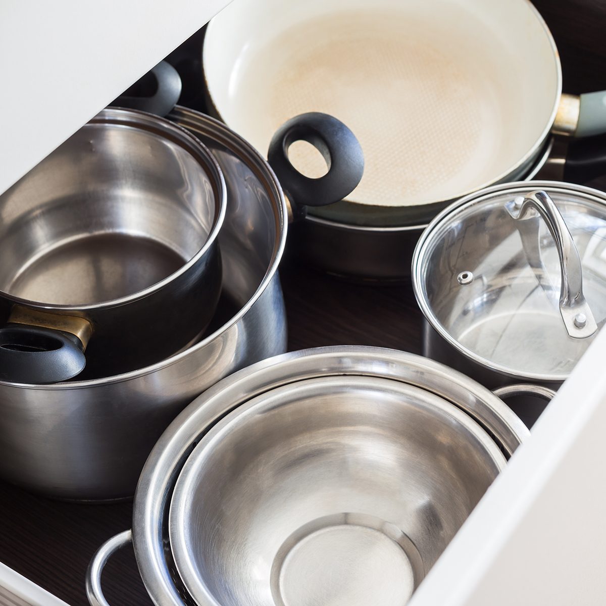Open drawer of cabinet with steel pots and pans and bowl.