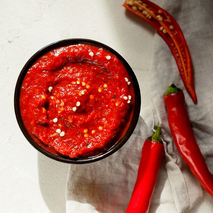 Traditional homemade rose harissa-hot chili pepper sauce paste with garlic and olive oil in small bowl on white plaster background