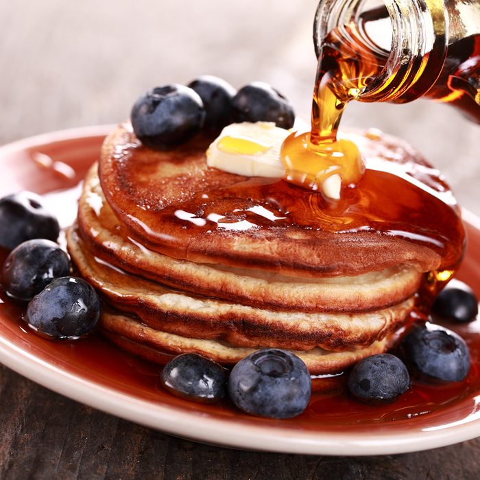 Pouring maple syrup on stack of pancakes