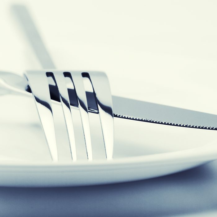 White plate, fork and knife on light background. Toned image.