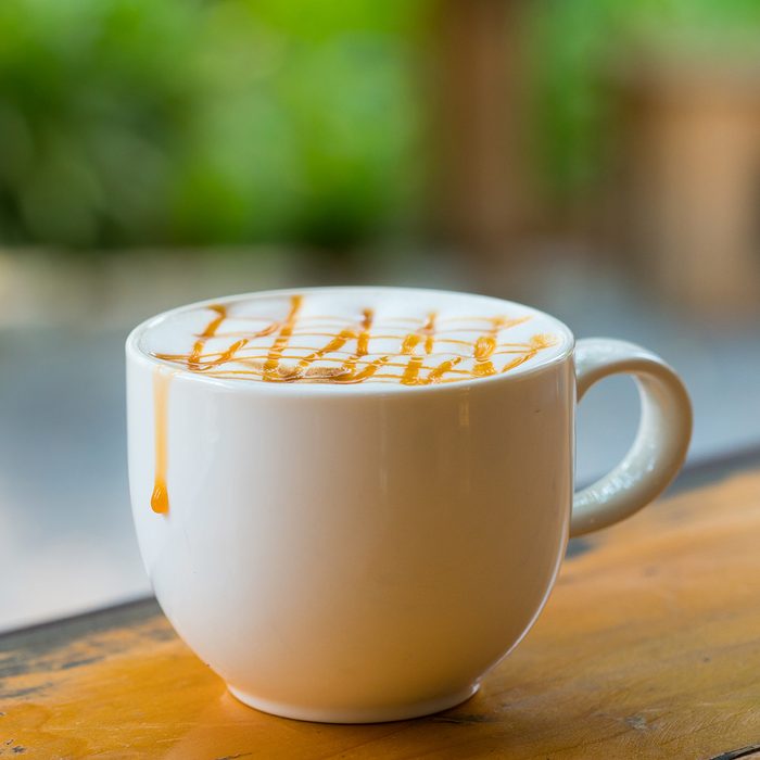 Hot Macchiato coffee with caramel in white cup on wood table by window light, copy-space background