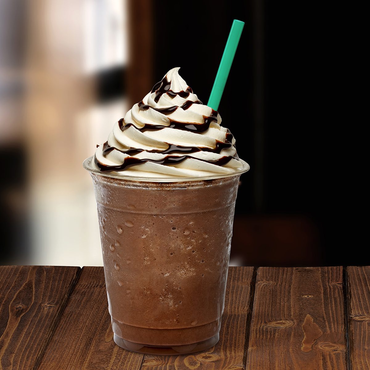 Frappuccino in takeaway cup on wooden table isolated on blackFrappuccino in takeaway cup on wooden table isolated on black