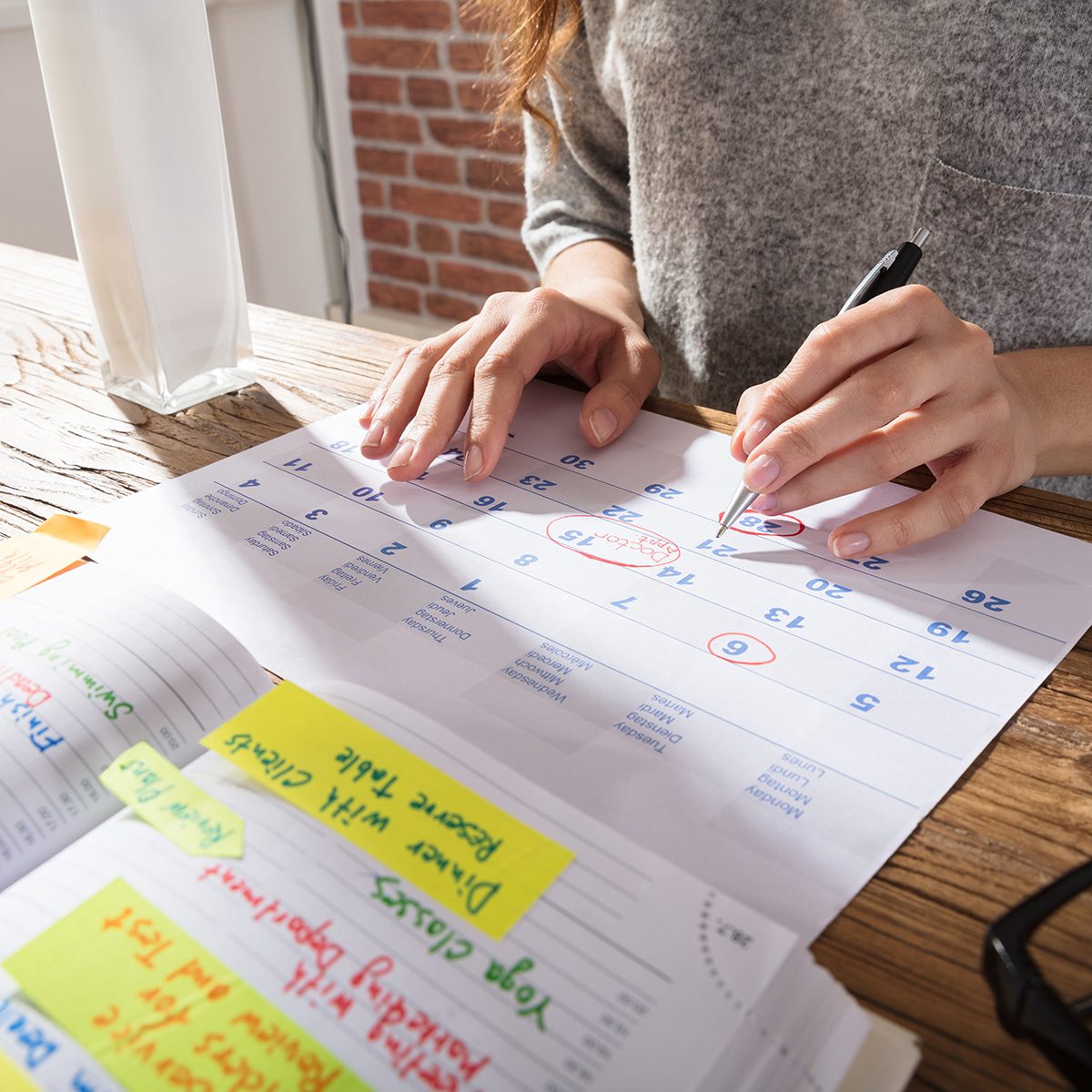 Close-up Of A Businesswoman Marking Schedule On Calendar From Diary At Workplace