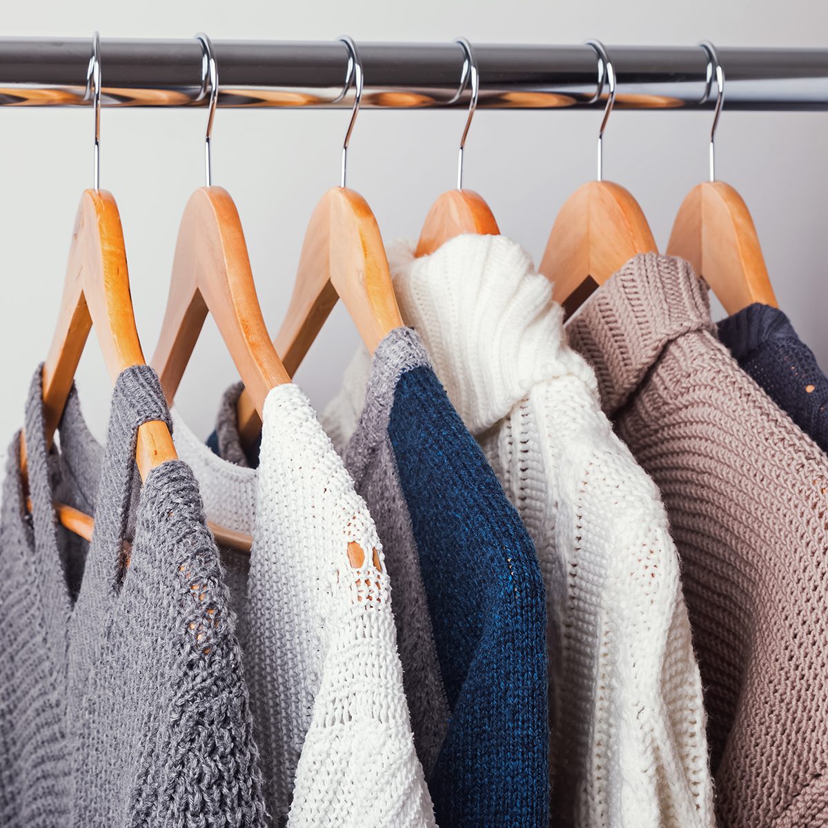 Different knitted sweaters on hangers close-up on the white wall background