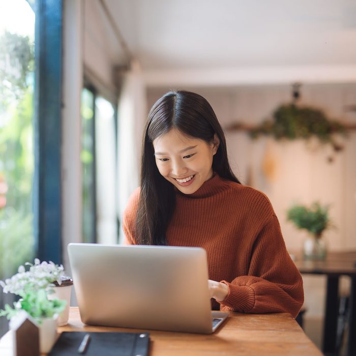 Happy young Asian girl working at a coffee shop with a laptop.
