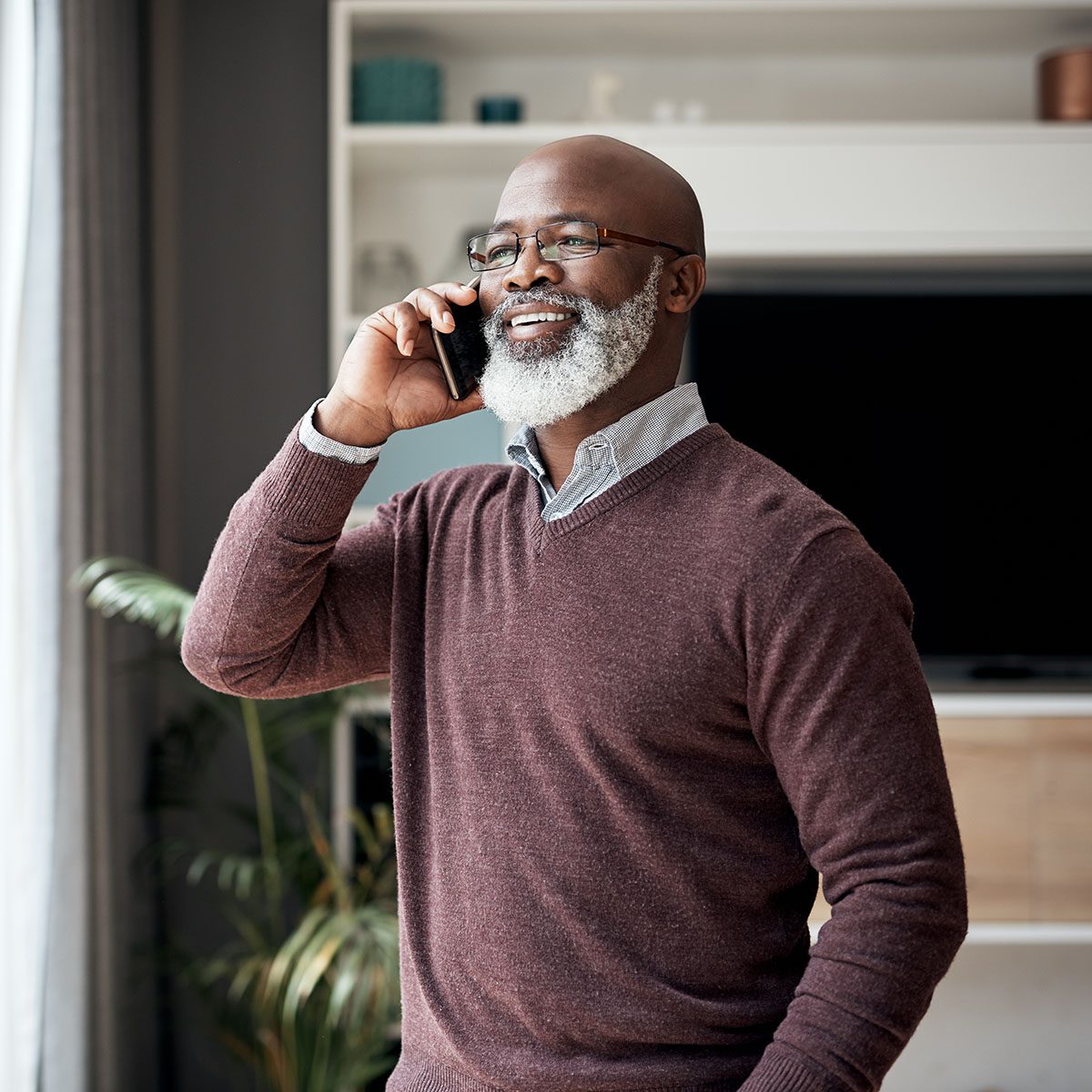 Cropped shot of a happy senior man standing alone in his living room at home and using his cellphone