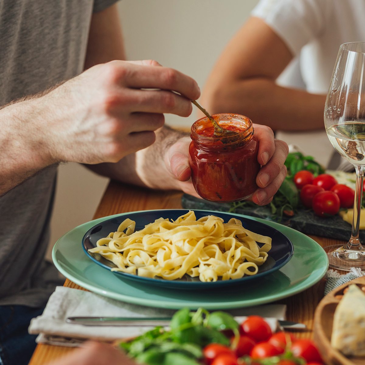 Hands of unrecognisable man holding a jar and putting sauce on his pasta at dinner.
