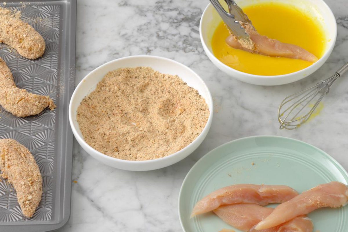 tongs dipping chicken tenders in egg and bread crumb