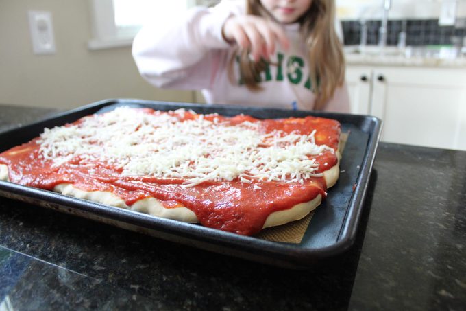 Child spreading cheese over sauce on pizza